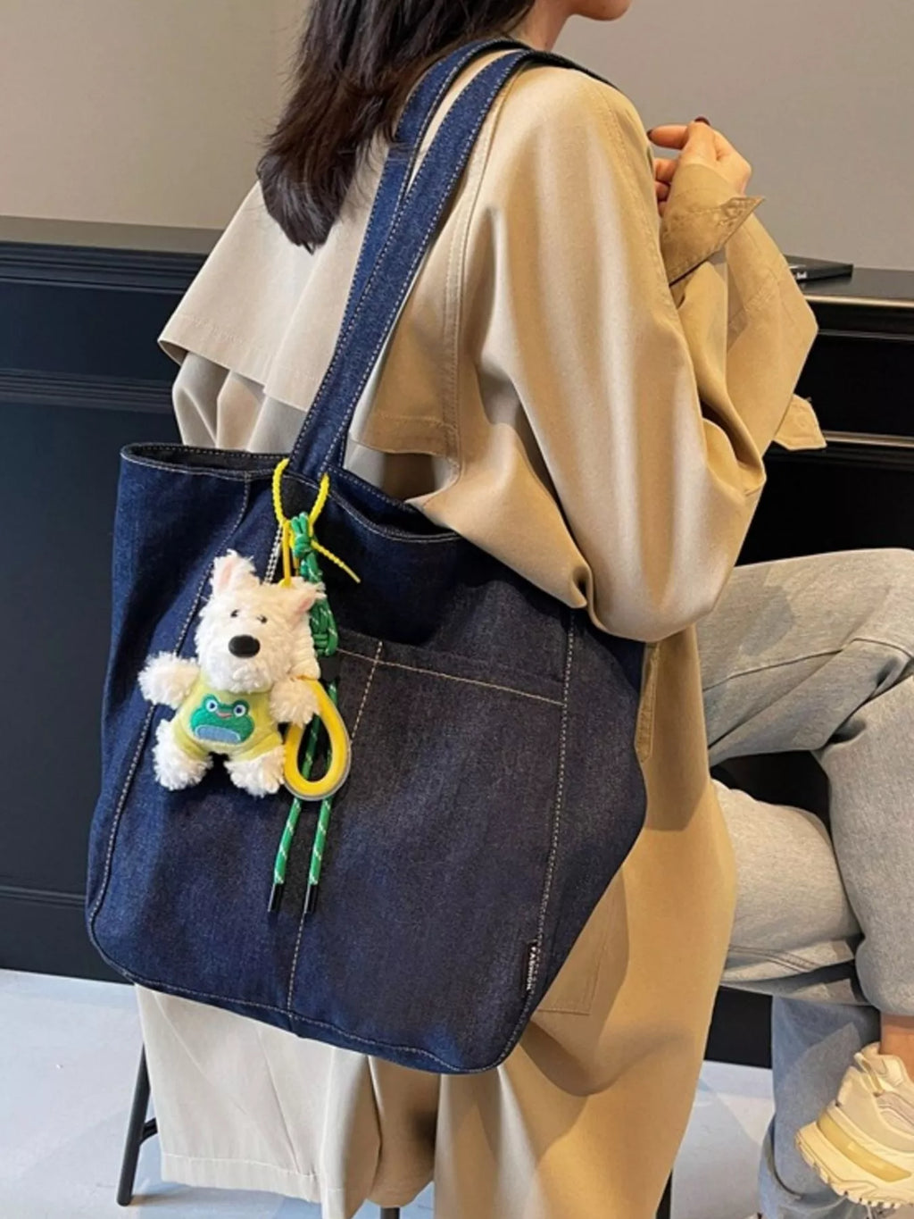 Denim shoulder tote on shoulder, dark navy with long straps and plush charm