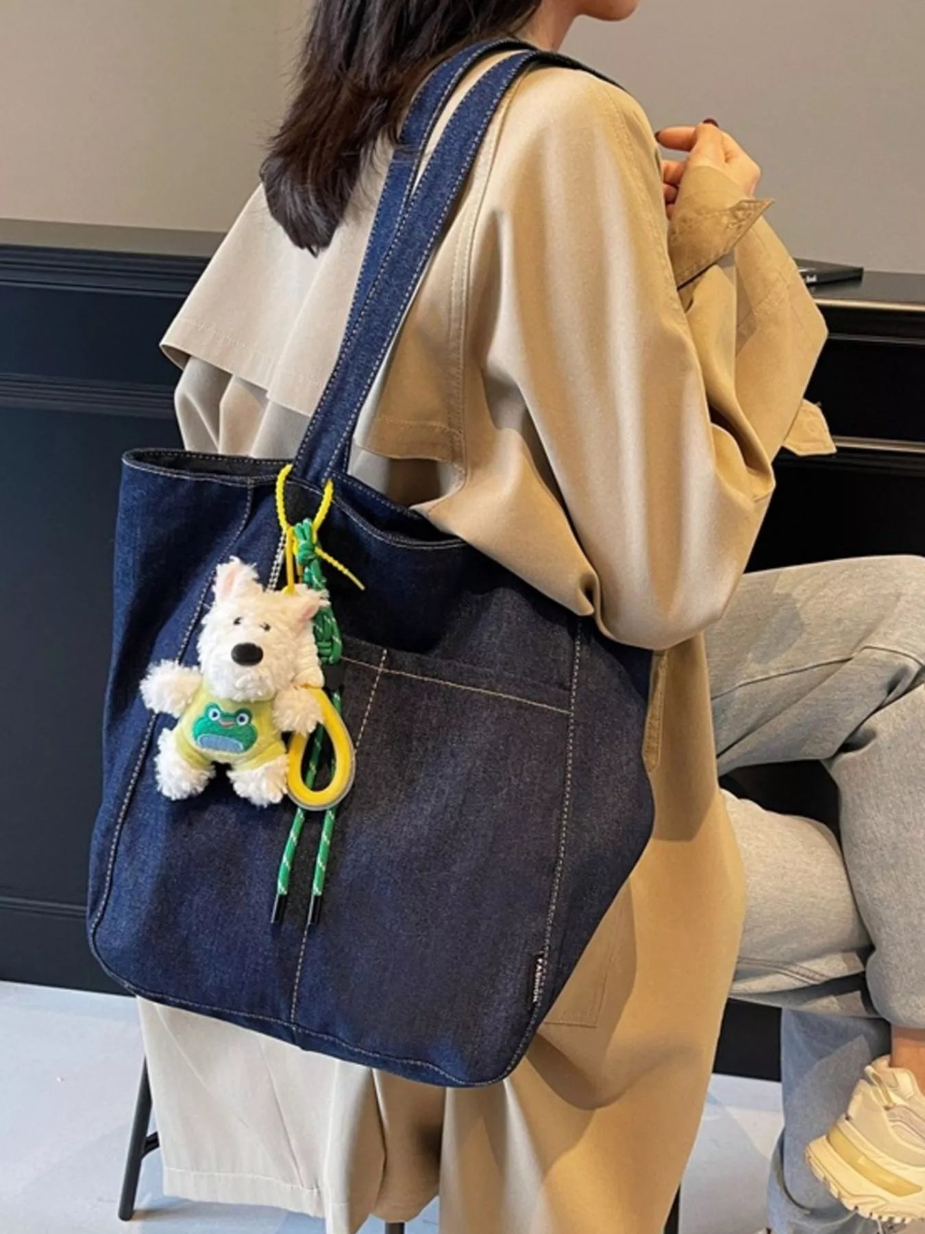 Denim shoulder tote on shoulder, dark navy with long straps and plush charm