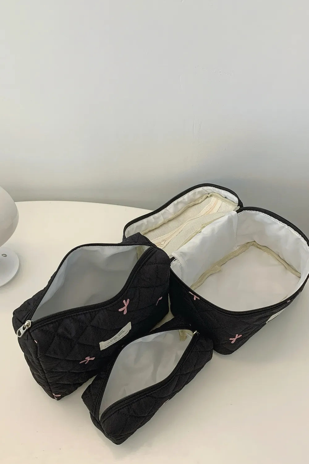 Black quilted storage bag set with bow print, open compartments showing beige lining.