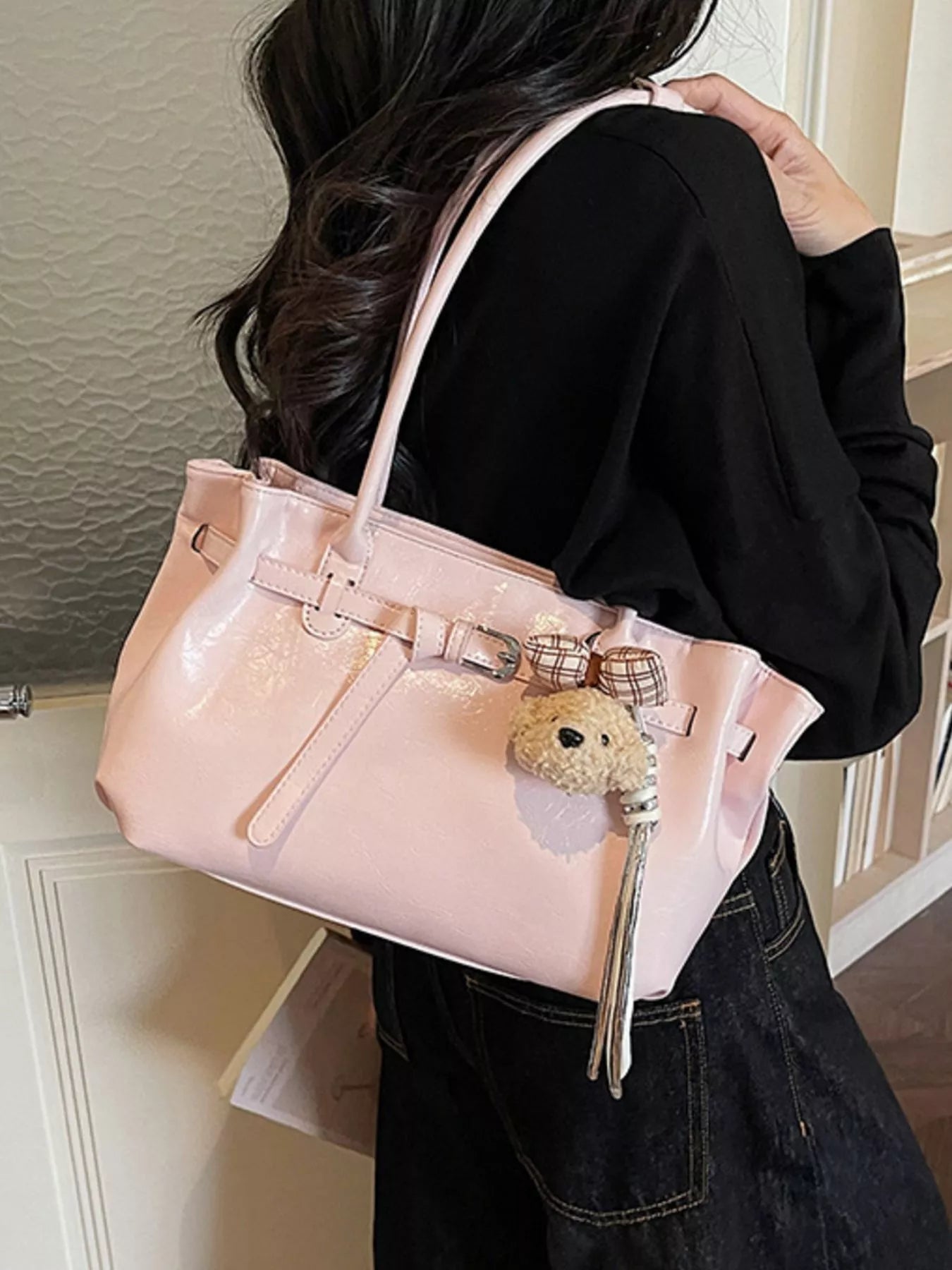 Blush pink leather shoulder bag worn on arm, dog charm front detail with tassel