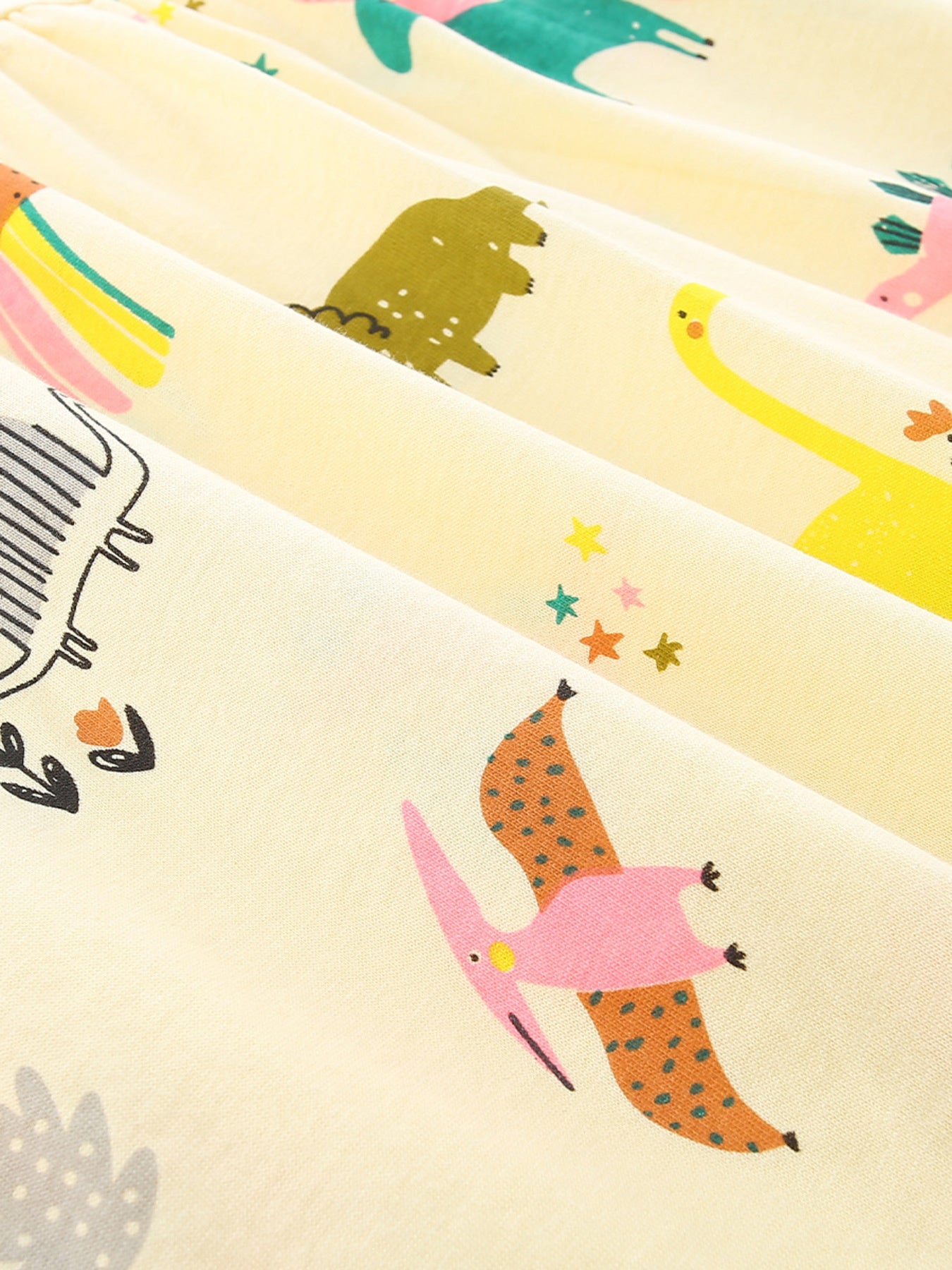 Fabric close-up: pastel yellow with colorful dinosaur illustrations