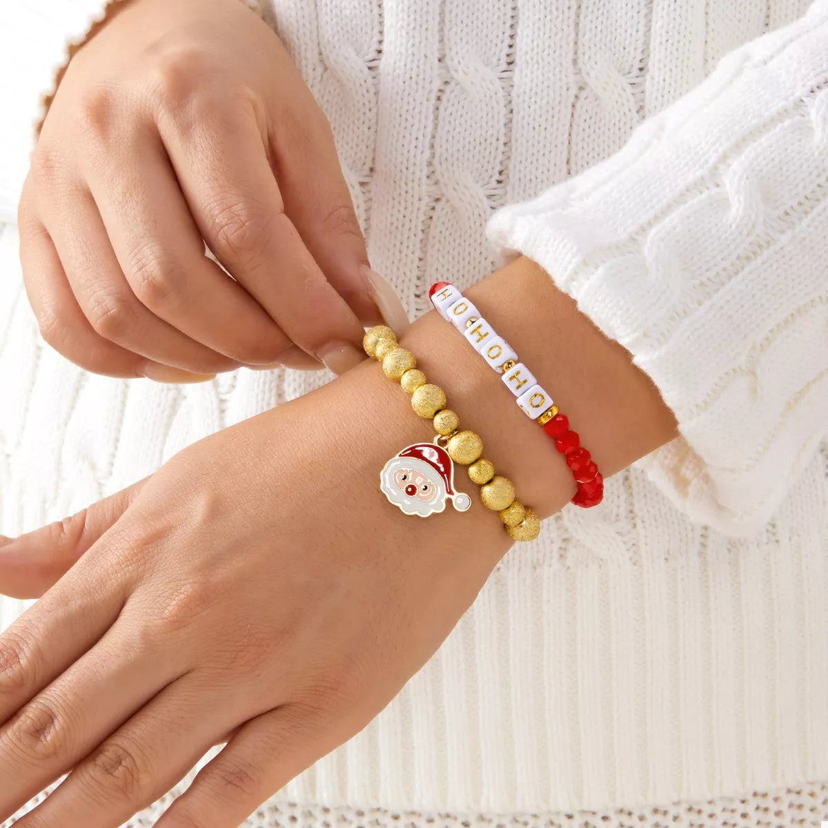 Stacked bracelets on hands: red HO HO HO bead strand, gold ball strand, Santa charm
