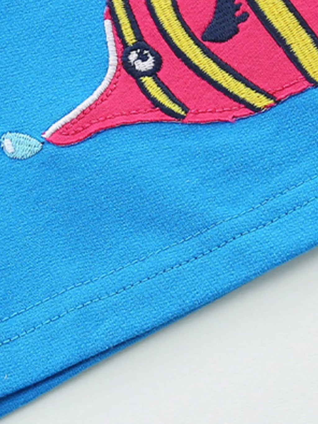 Blue shorts hem close-up with embroidered fish patch and visible stitching along cuff