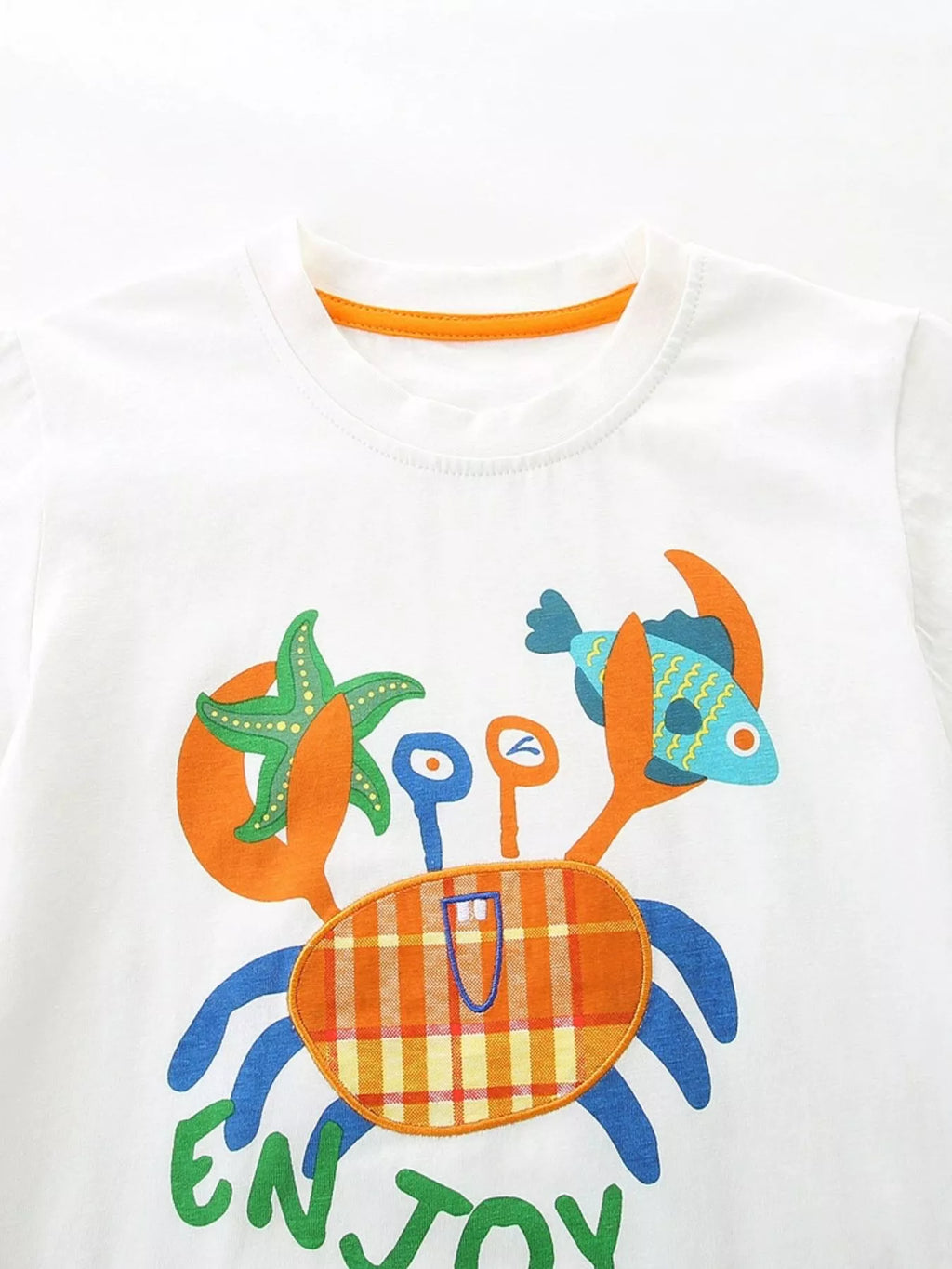 White tee close-up: colorful crab graphic over checkered bib, “ENJOY TODAY” text