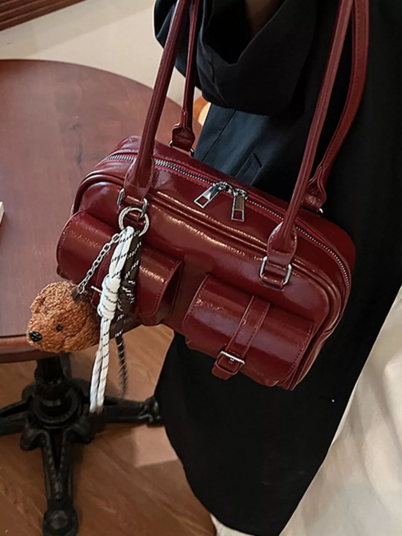 Deep red patent shoulder bag with top zipper, layered panels, and front buckle detail