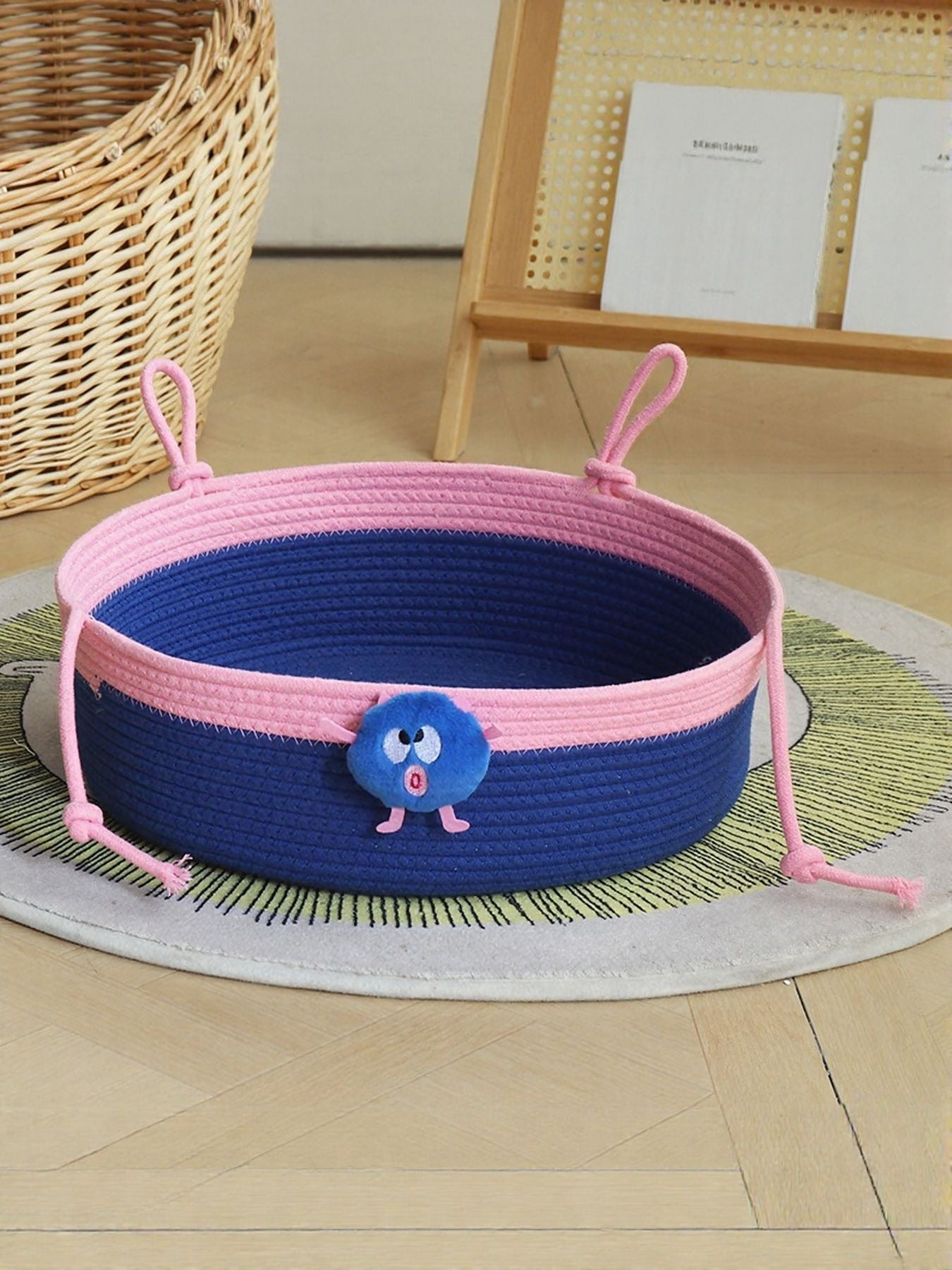 Two-tone woven pet nest with blue body, pink rim, and plush monster toy in center