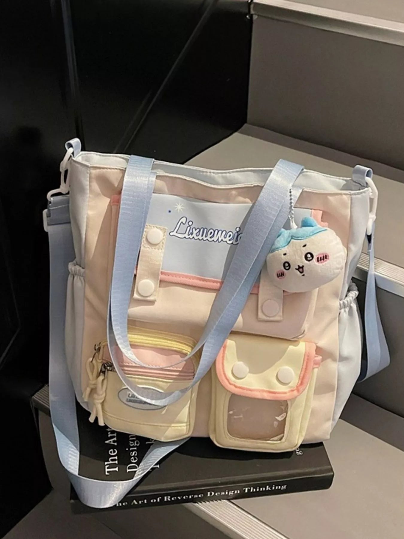 Multi-pocket shoulder bag with pastel blue straps, plush charm, and multiple zip pockets
