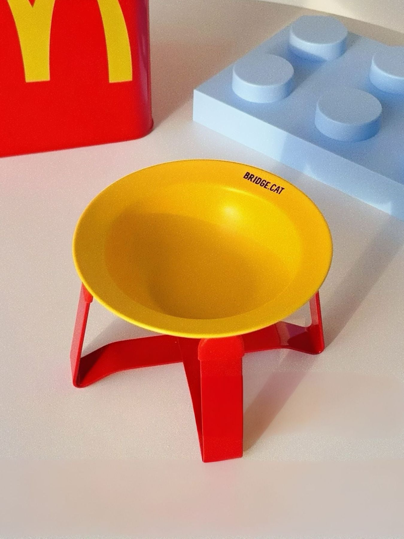 Yellow pet food bowl on red stand with small text on the rim