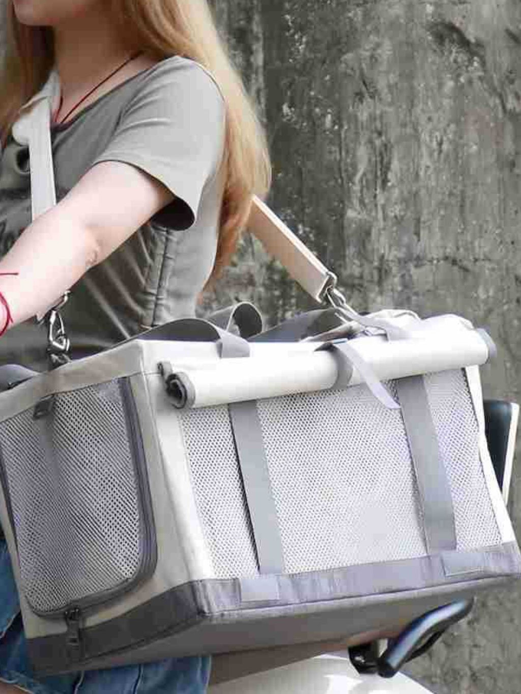 Portable gray pet carrier bag carried by a person, with rolled top and front mesh.