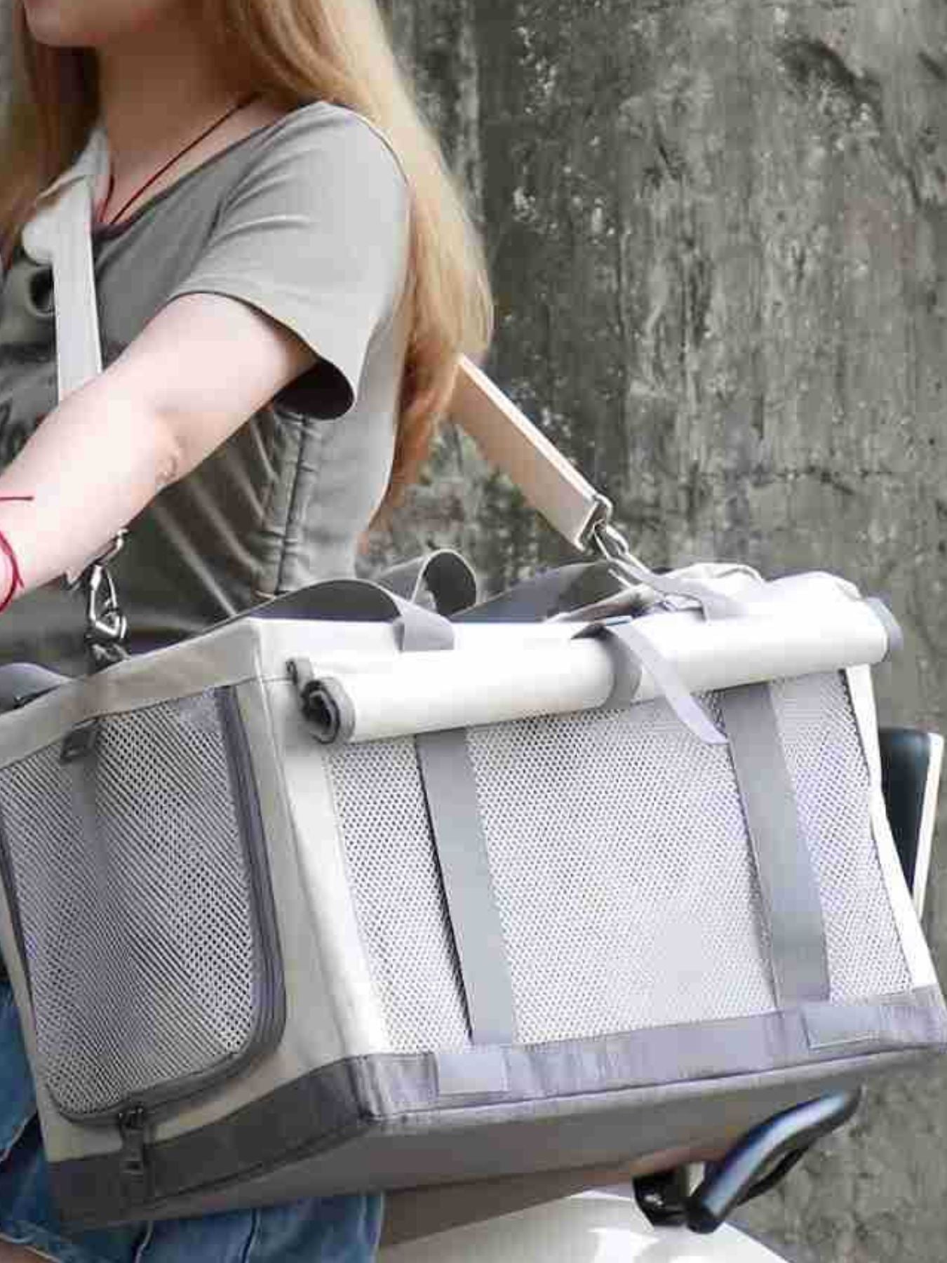 Portable gray pet carrier bag carried by a person, with rolled top and front mesh.