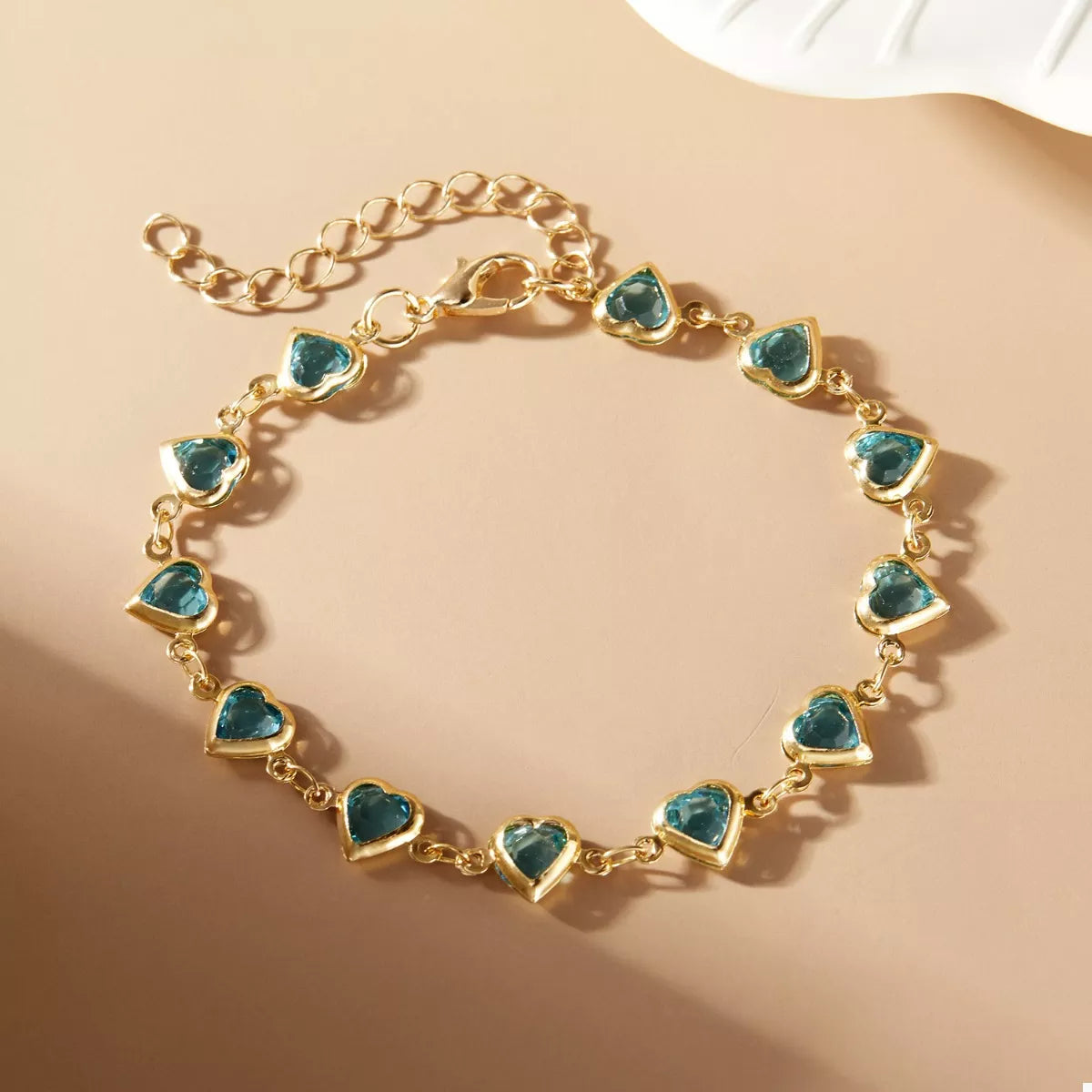 Gold-plated heart bracelet with teal heart charms and linked chain, round clasp view