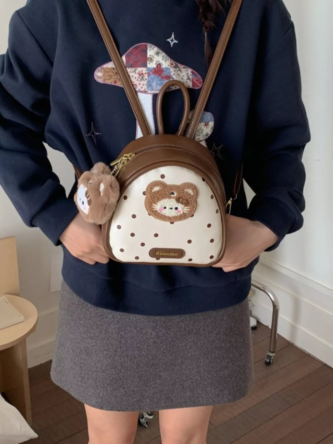 Cartoon Bear Backpack Bag held in hands, brown with bear patch and dotted white front panel