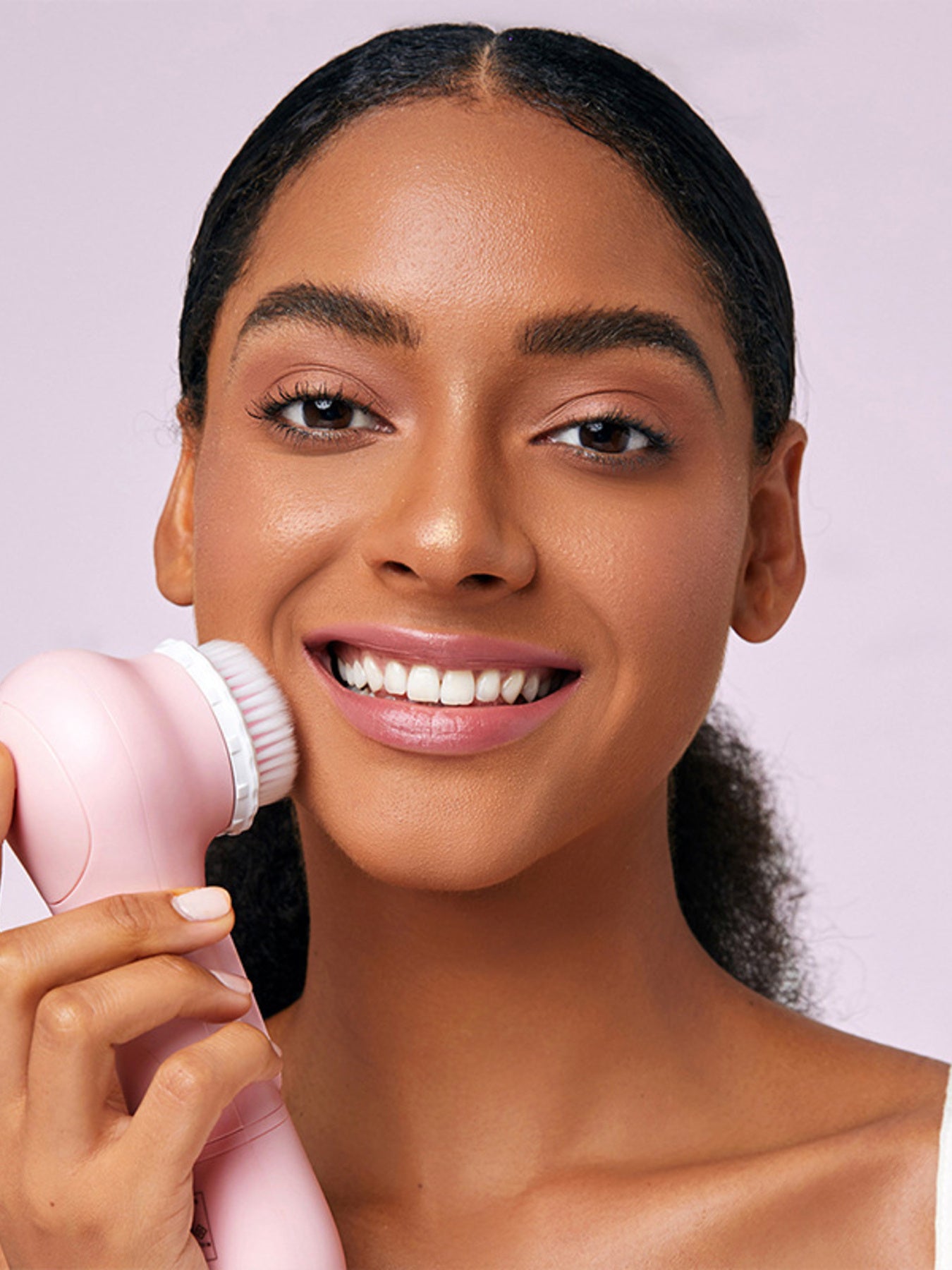 Rotating facial cleansing brush against face, pink handle and round bristles