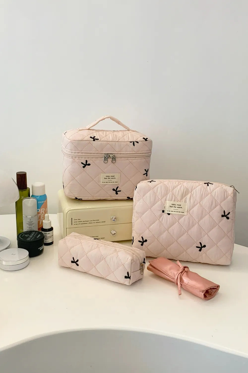 Light pink quilted 3-piece storage bag set with bow print, zip tops, and labels.